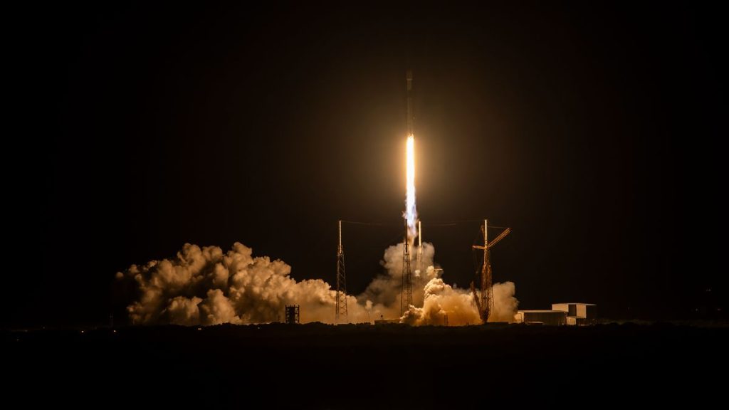 a black-and-white spacex falcon 9 rocket launches into a night sky.