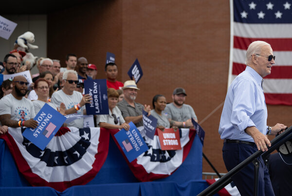 President Biden climbs a staircase as people hold union signs cheer behind him.