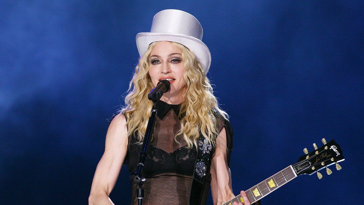 Madonna indossa un cappello bianco e suona la chitarra in concerto