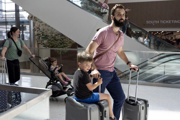 George Ridley, 4 anni, a sinistra, viaggia su una valigia mentre lui e suo padre, Chris Ridley, attraversano l'aeroporto internazionale di Nashville, giovedì 23 maggio 2024, a Nashville, Tennessee.  Si prevede che un numero record di americani viaggeranno durante il weekend del Memorial Day 2024. (AP Photo/George Walker IV)