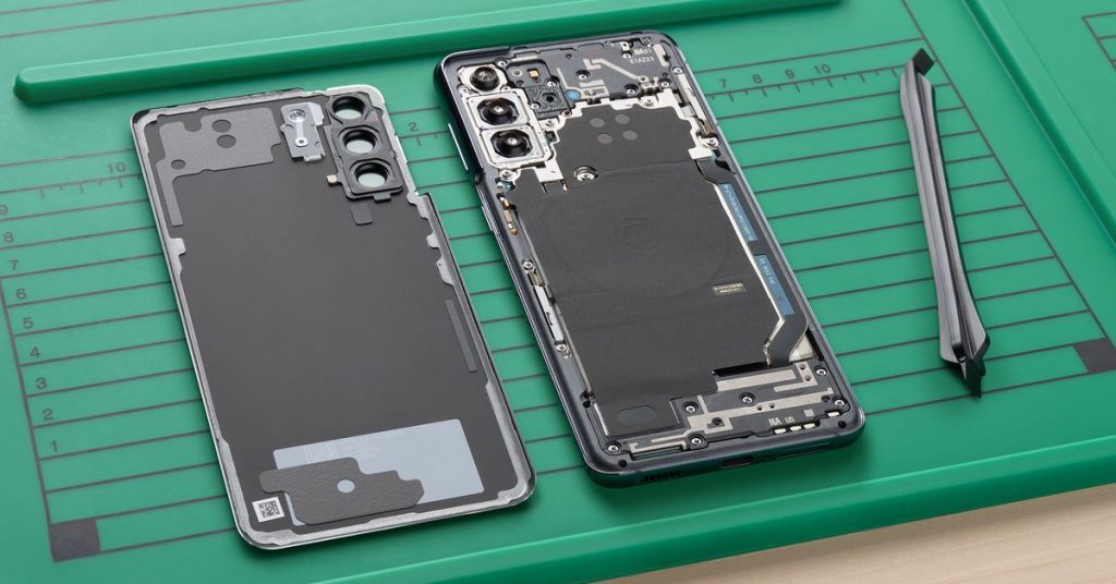 A Samsung phone, opened up, on a green background, with a spudger tool next to it.