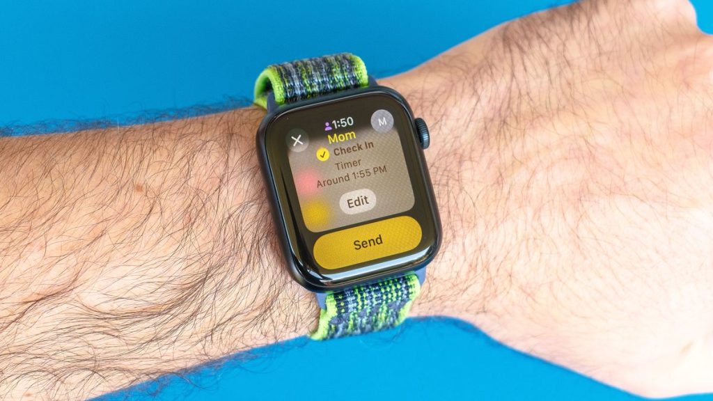 Detail shot of an Apple Watch SE on a bright blue background showing the steps to set up and send a Check In notification in watchOS 11