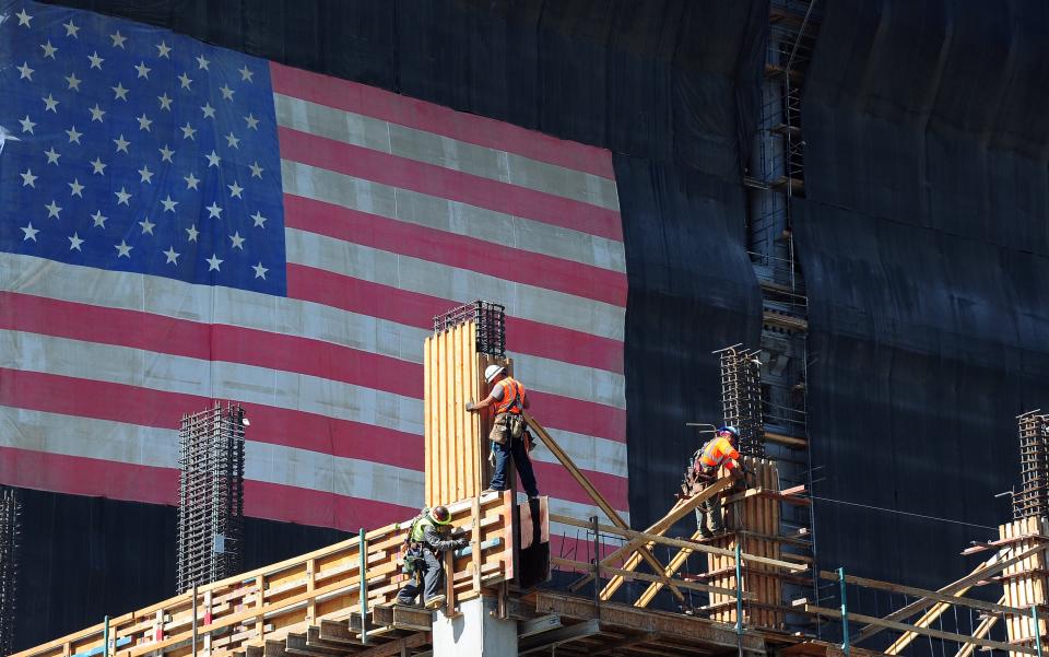 Operai edili lavorano su un nuovo edificio parzialmente coperto da una grande bandiera americana il 25 settembre 2013 a Los Angeles, California, mentre il governatore Jerry Brown firmava la legislazione che aumenterà il salario minimo della California da 8 a 10 dollari l'ora entro il 2016. Foto AFP/ Frederick J. Brown (il credito fotografico dovrebbe essere Frederick J. Brown/AFP tramite Getty Images).