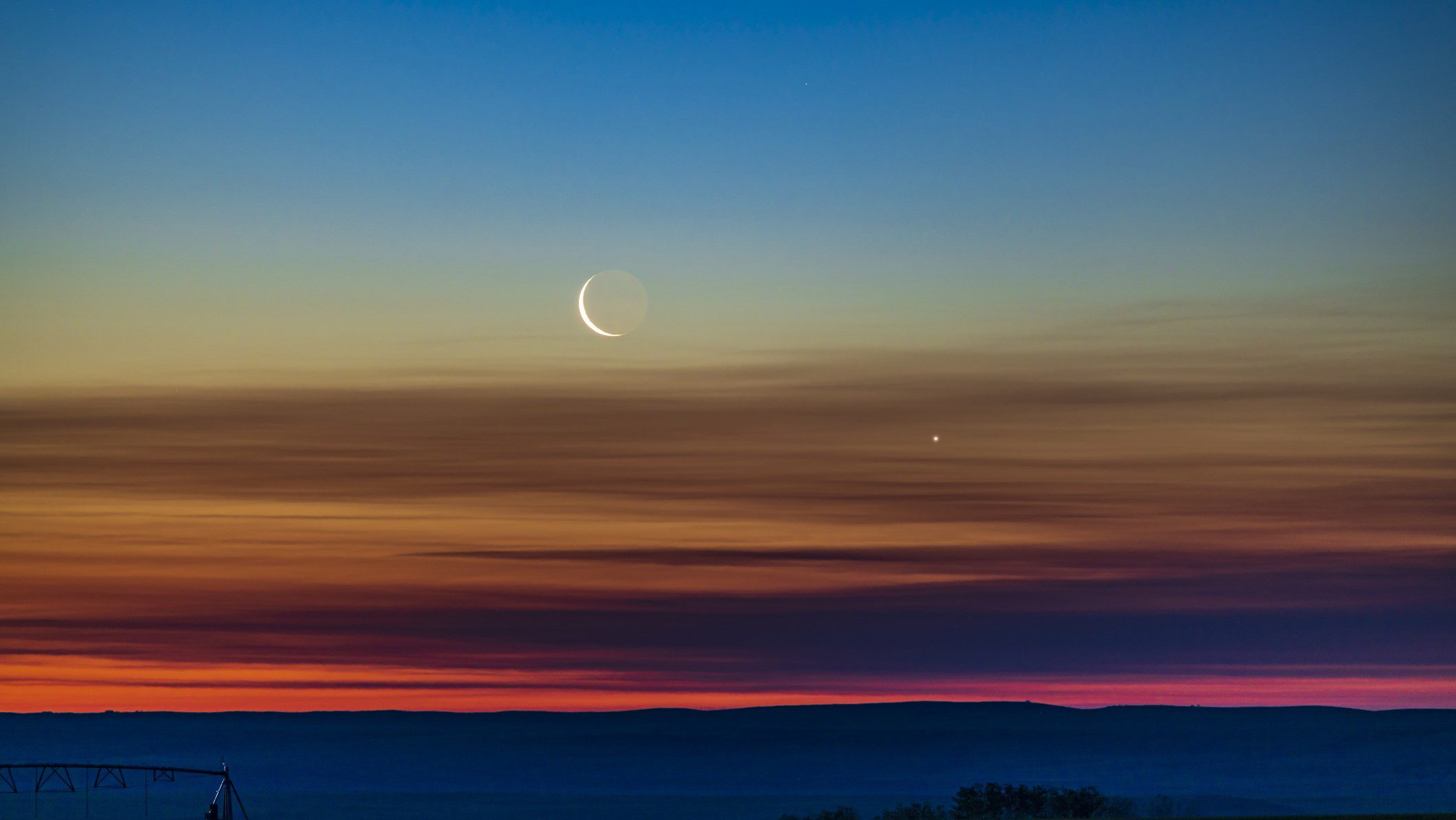 La congiunzione della mezzaluna calante e di Venere mentre sorgono nel cielo dell'alba nord-orientale nel sud dell'Alberta, in Canada.  La luce della Terra può essere vista sul lato oscuro della Luna.  Il cielo mostra una meravigliosa transizione di colori dall'arancione all'orizzonte attraverso tutto lo spettro al blu nella parte superiore