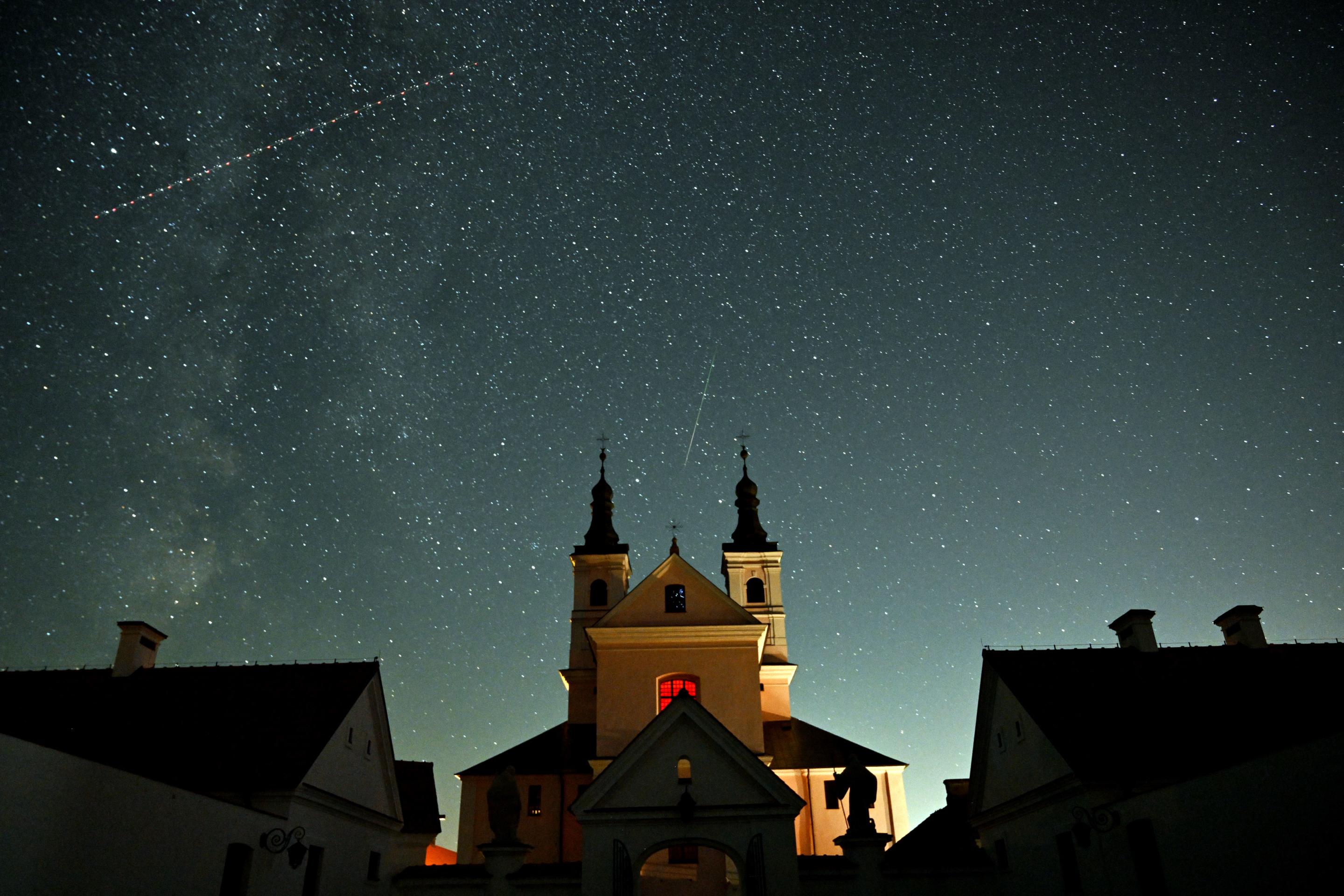 Una meteora, al centro, può essere vista come un satellite che attraversa il cielo notturno sopra un monastero nella regione di Suwalki in Polonia.