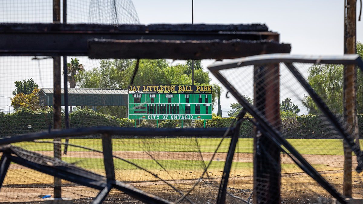 I resti bruciati delle storiche gradinate e panchine in legno incorniciano una vista del tabellone segnapunti dopo che un incendio nella tarda mattinata di giovedì ha distrutto lo storico campo da baseball del Jay Littleton Ball Park in Ontario, California.